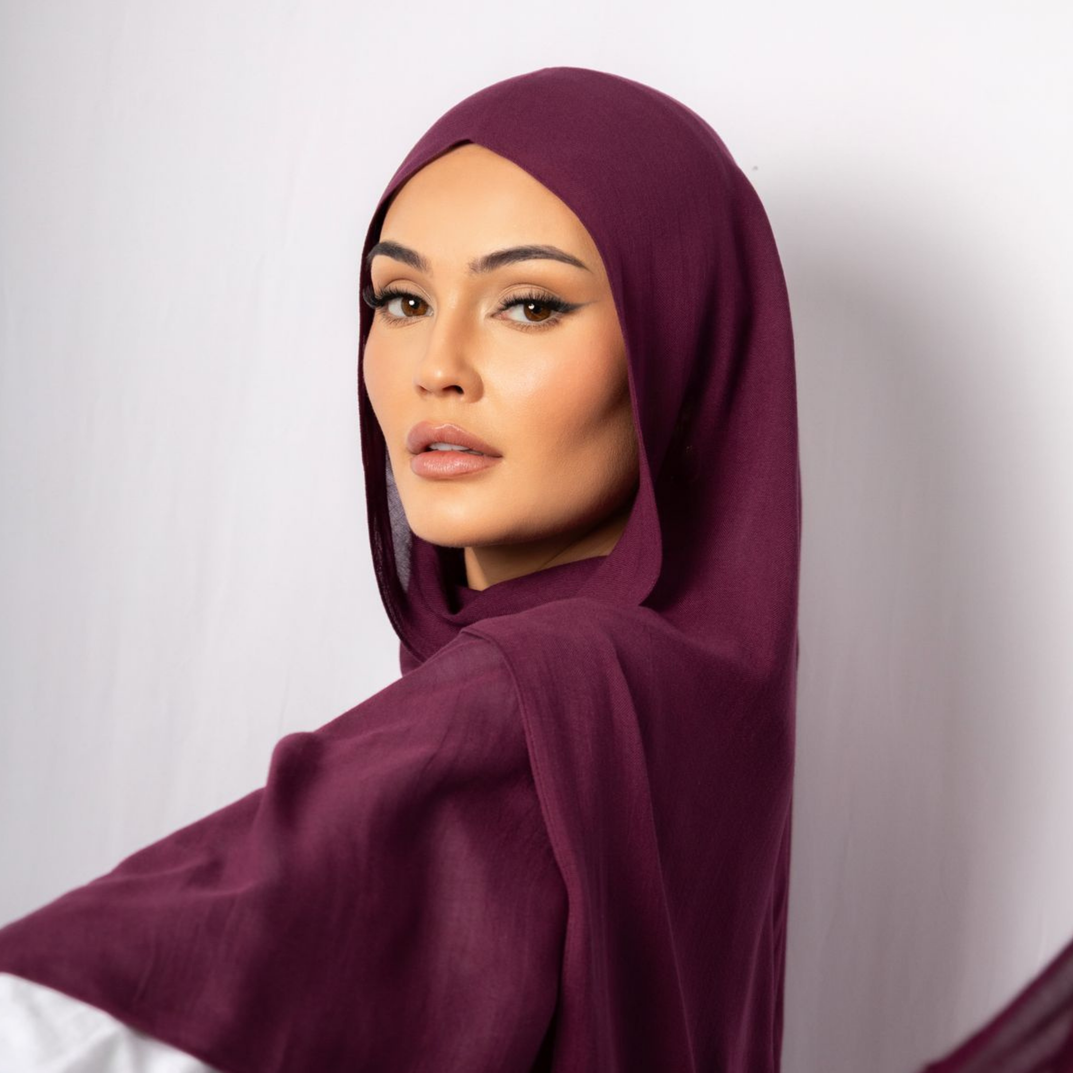 Woman wearing a deep plum hijab posing gracefully with flowing fabric, showcasing elegant modest fashion on a clean studio background