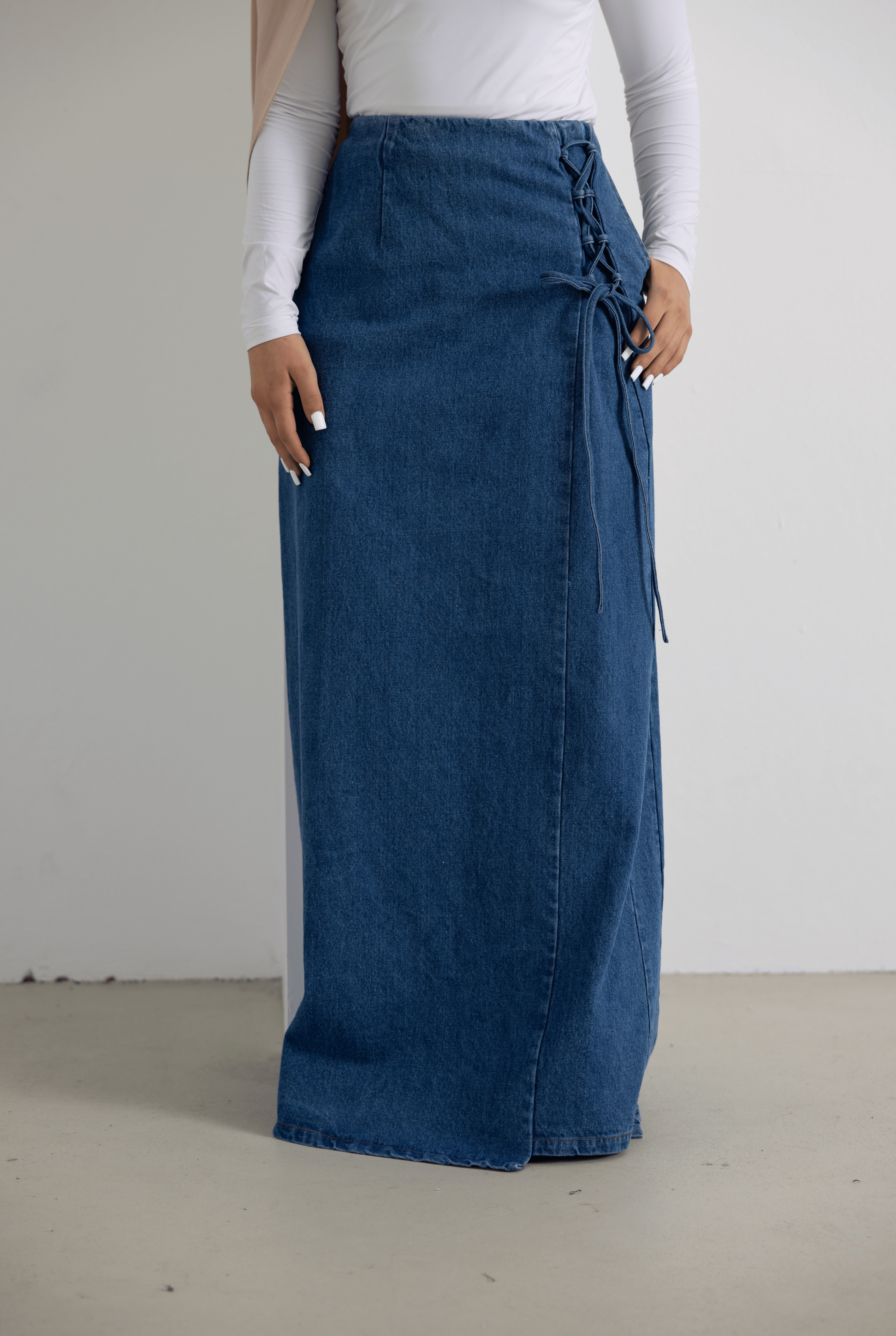 Front view of the Lace Denim Skirt in mid-wash denim blue, featuring a modest longline silhouette, clean front seam, and feminine lace-up side detailing. Crafted from 100% cotton with a structured yet comfortable fit, making it a versatile denim skirt for everyday wear and elevated casual styling.