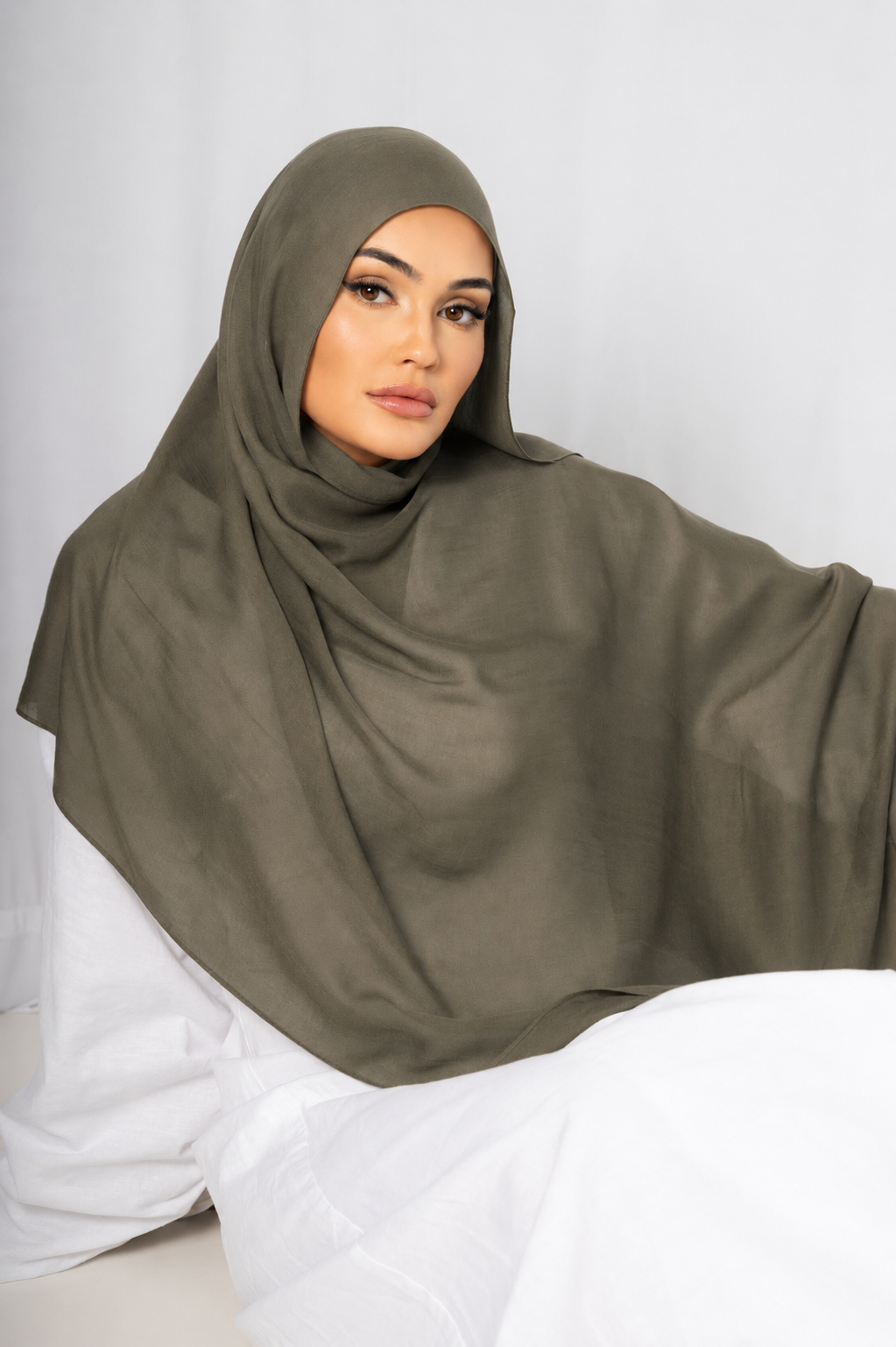 Model wearing the Olive Grove modal hijab in a seated front view, showcasing its earthy olive green shade, lightweight breathable fabric, soft drape, and elegant modest styling