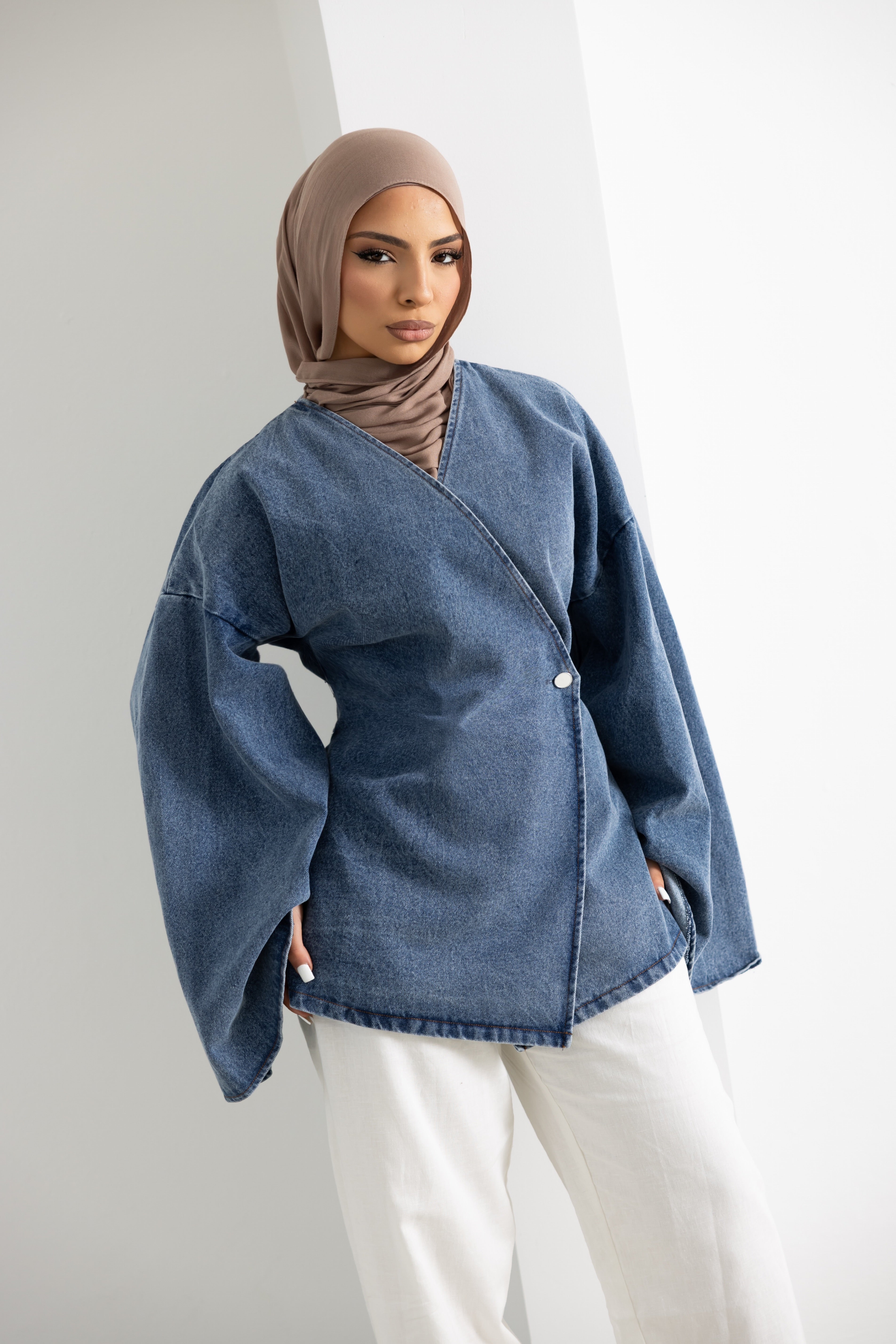 Close-up front view of the Orlena Signature Denim Mini jacket crafted from 100% cotton with a soft denim-look finish. Features a flattering wrap-style front, wide statement sleeves, adjustable back tie waist, and mini-length silhouette. Elegant modest fashion jacket styled with wide-leg pants for a contemporary and versatile everyday look.
