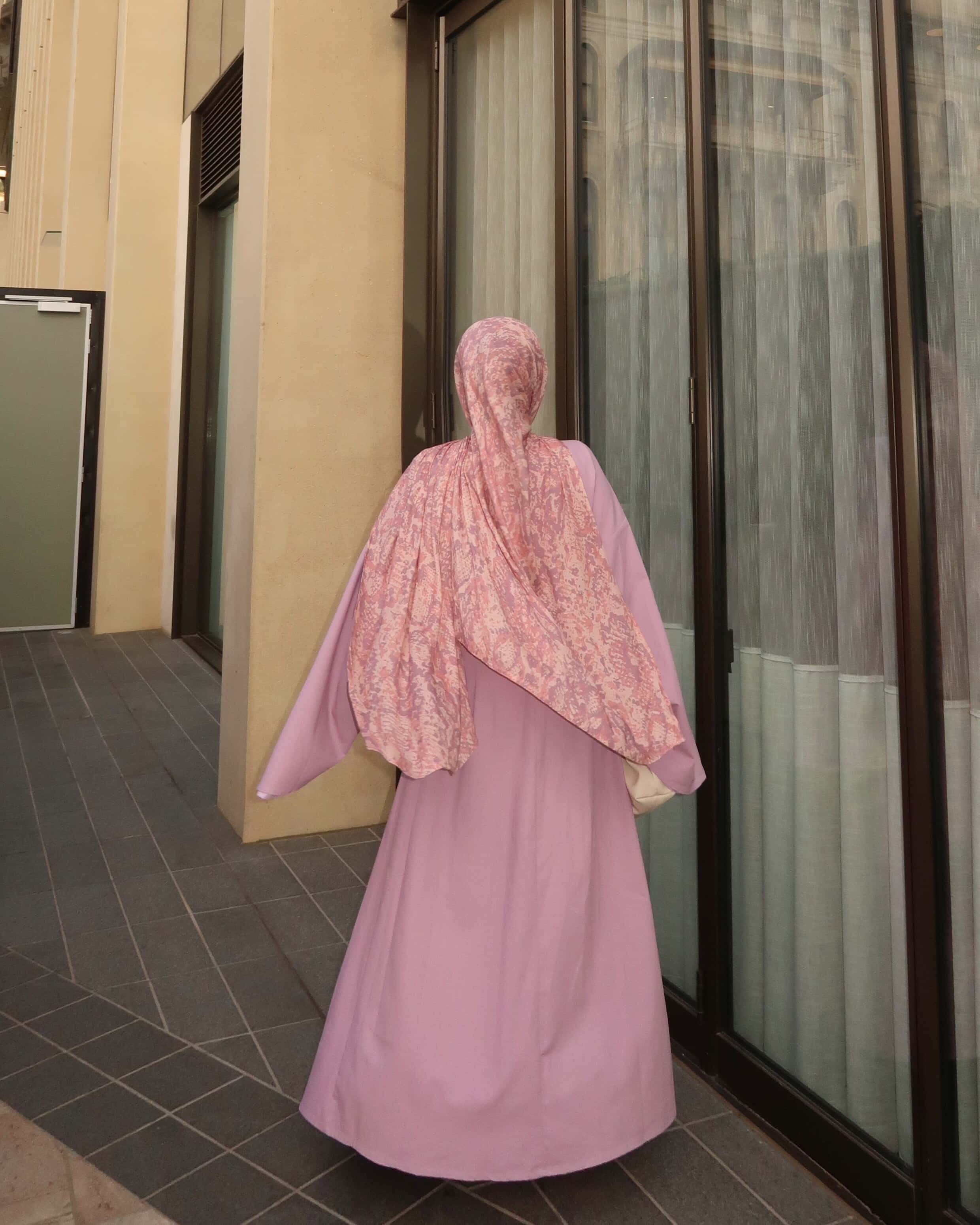 Woman wearing a pink modest maxi dress with patterned hijab standing outdoors in elegant modest fashion style