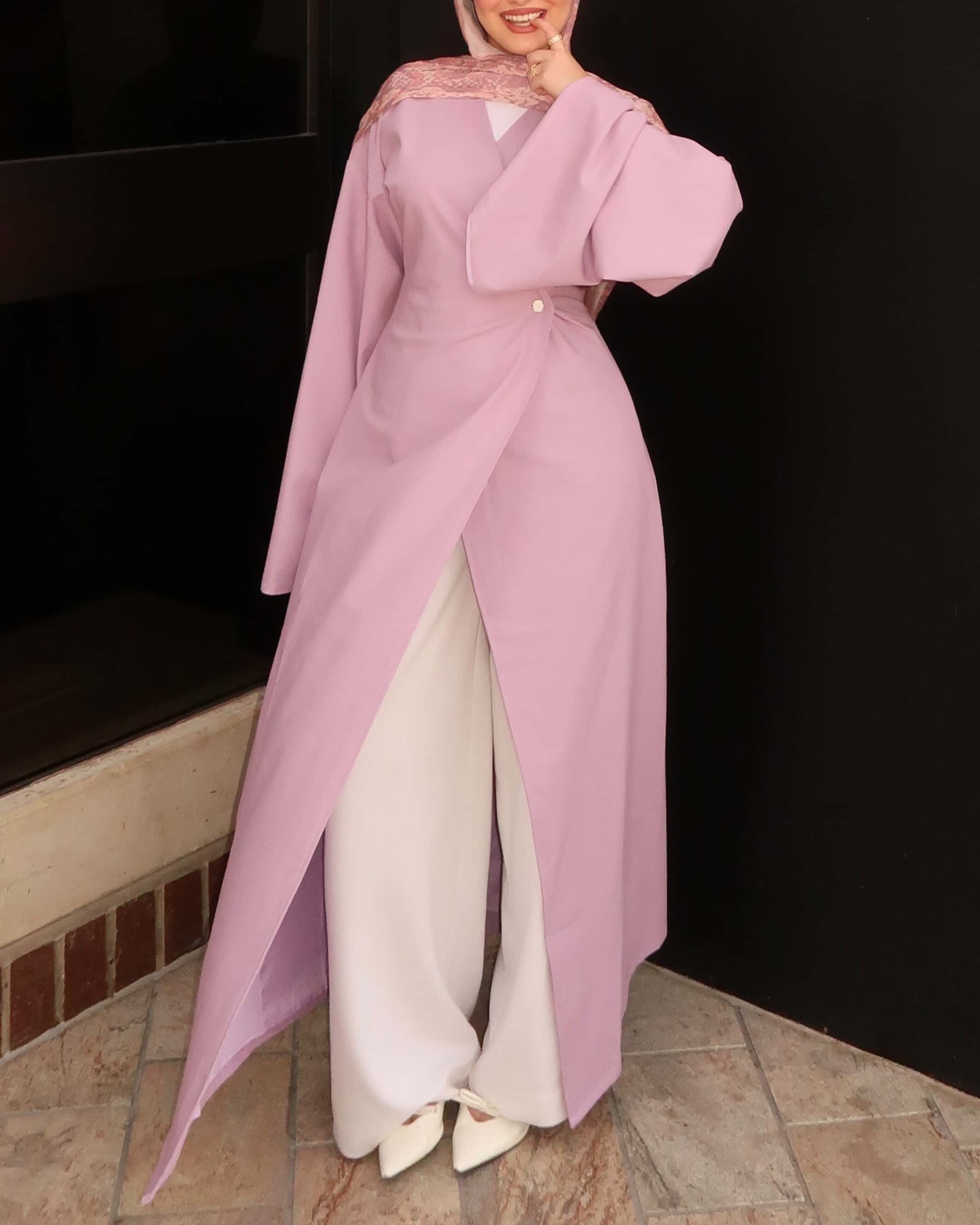 Woman wearing a pink modest wrap dress with hijab and white wide-leg pants in an elegant modest fashion outfit