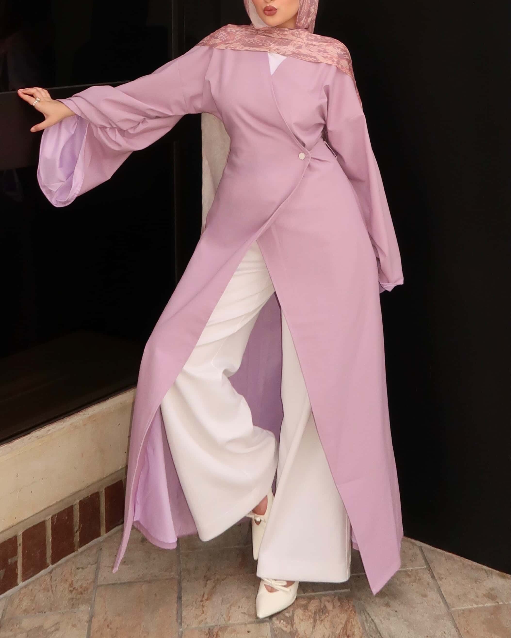 Woman wearing a pink modest wrap dress with patterned hijab and white pants captured in motion in an elegant modest fashion outfit