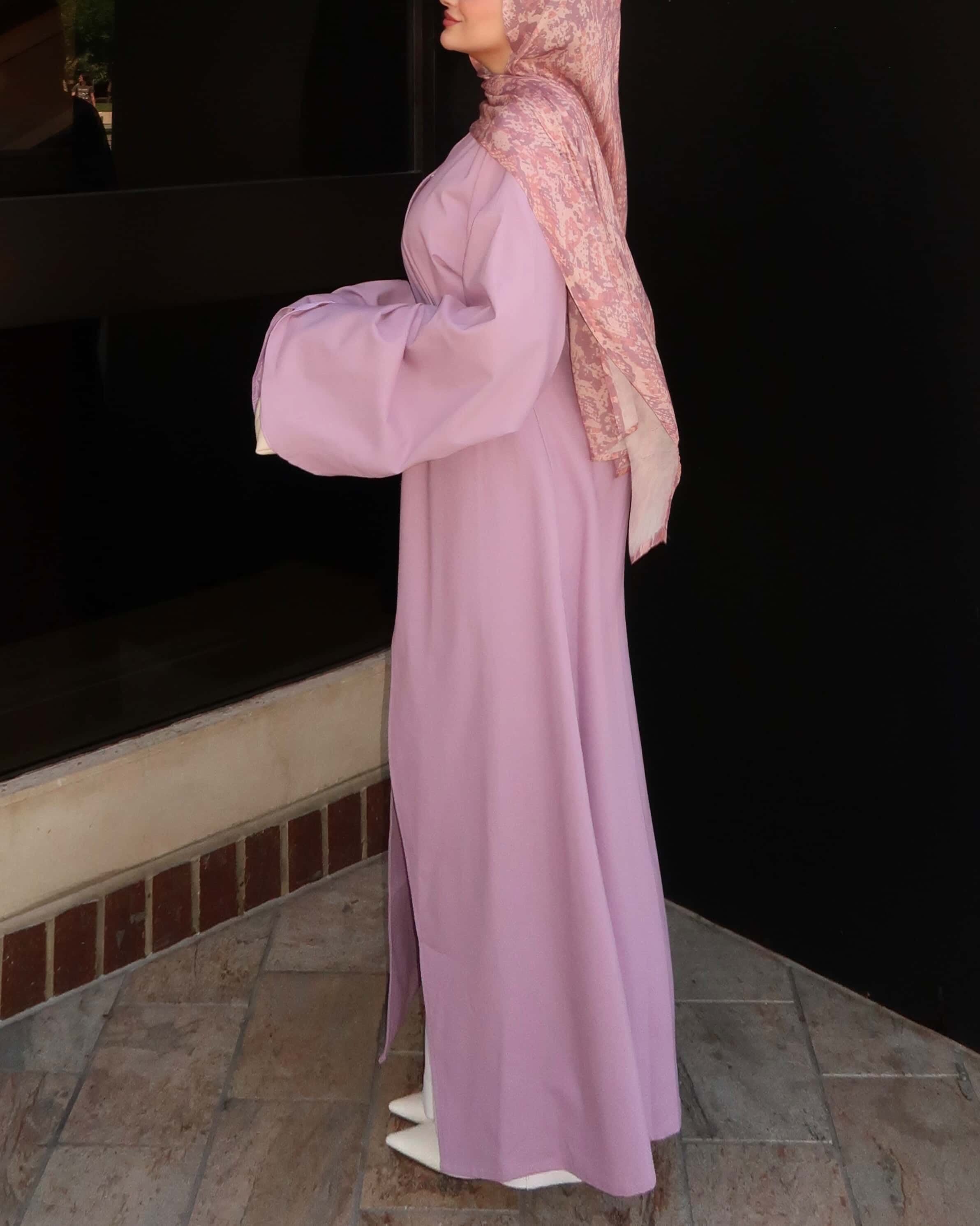 Side view of a woman wearing a pink modest wrap dress with patterned hijab in an elegant modest fashion outfit