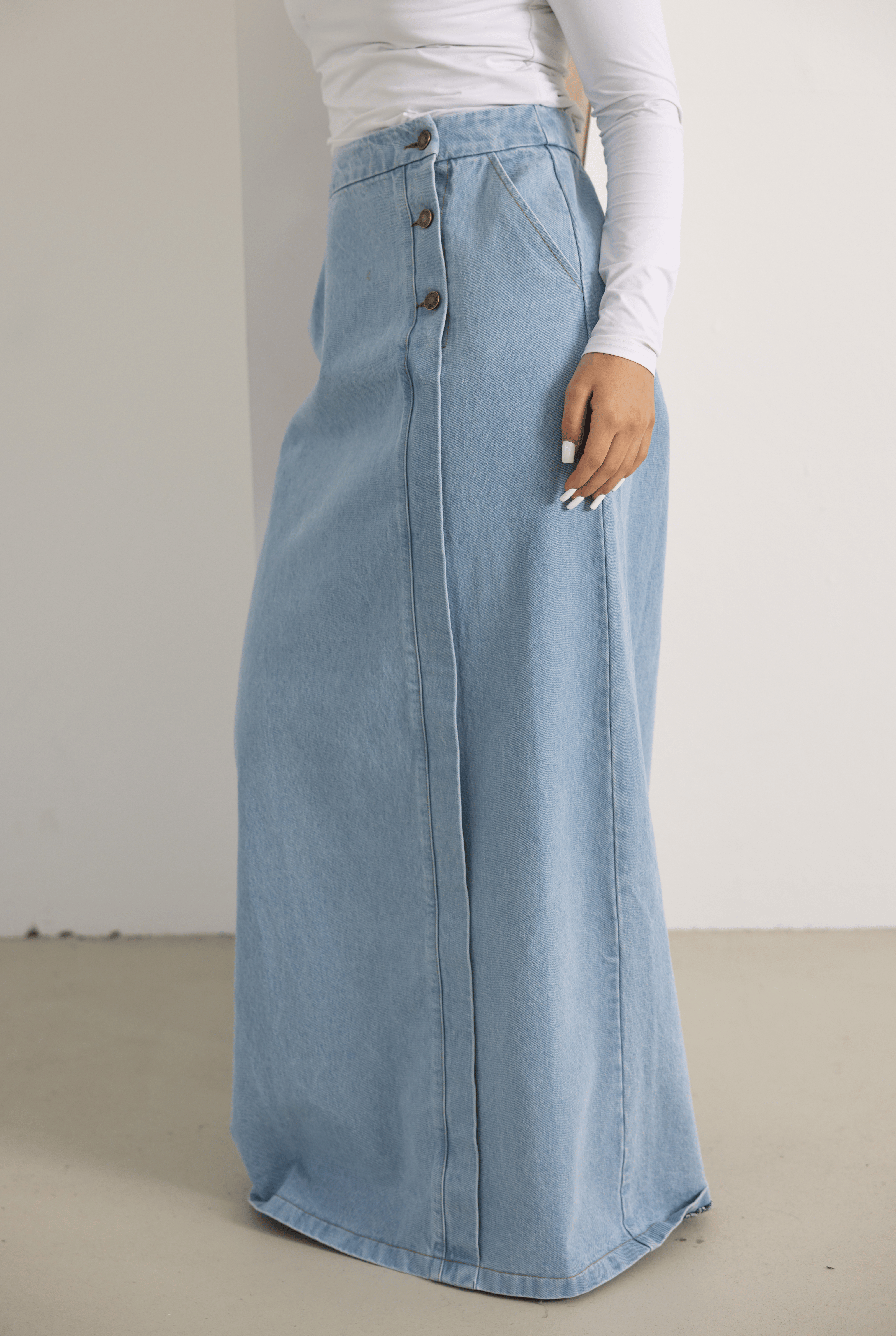 Front view of the Side Button Denim Skirt in light denim blue, featuring a modest longline silhouette, side button detailing, and a soft A-line shape. Made from 100% cotton with a structured yet comfortable feel, this timeless denim skirt is perfect for everyday styling and elevated casual outfits.