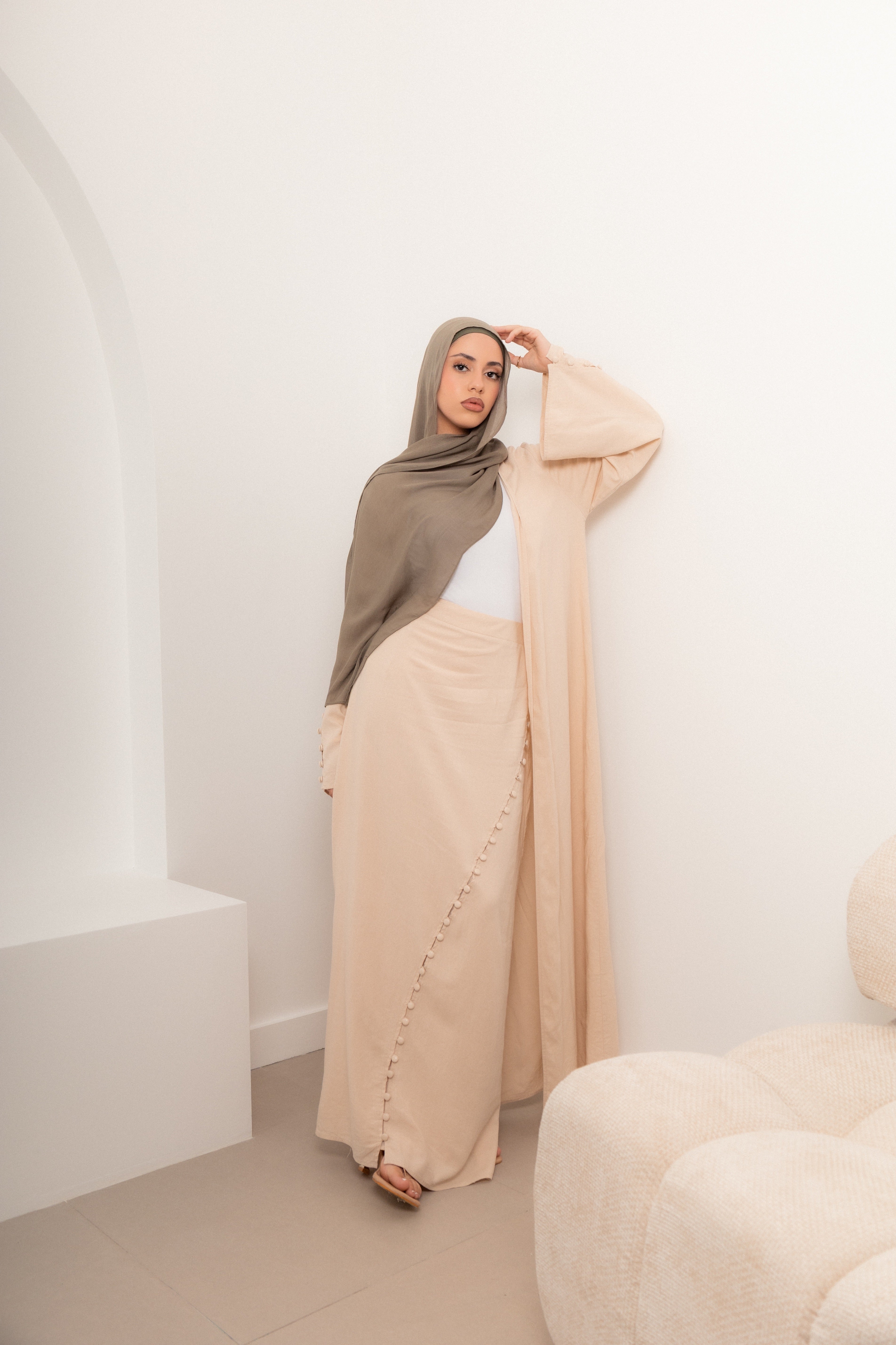 Woman wearing a soft neutral modest outfit with a hijab and flowing maxi skirt, styled in a minimalist interior for an elegant, effortless look