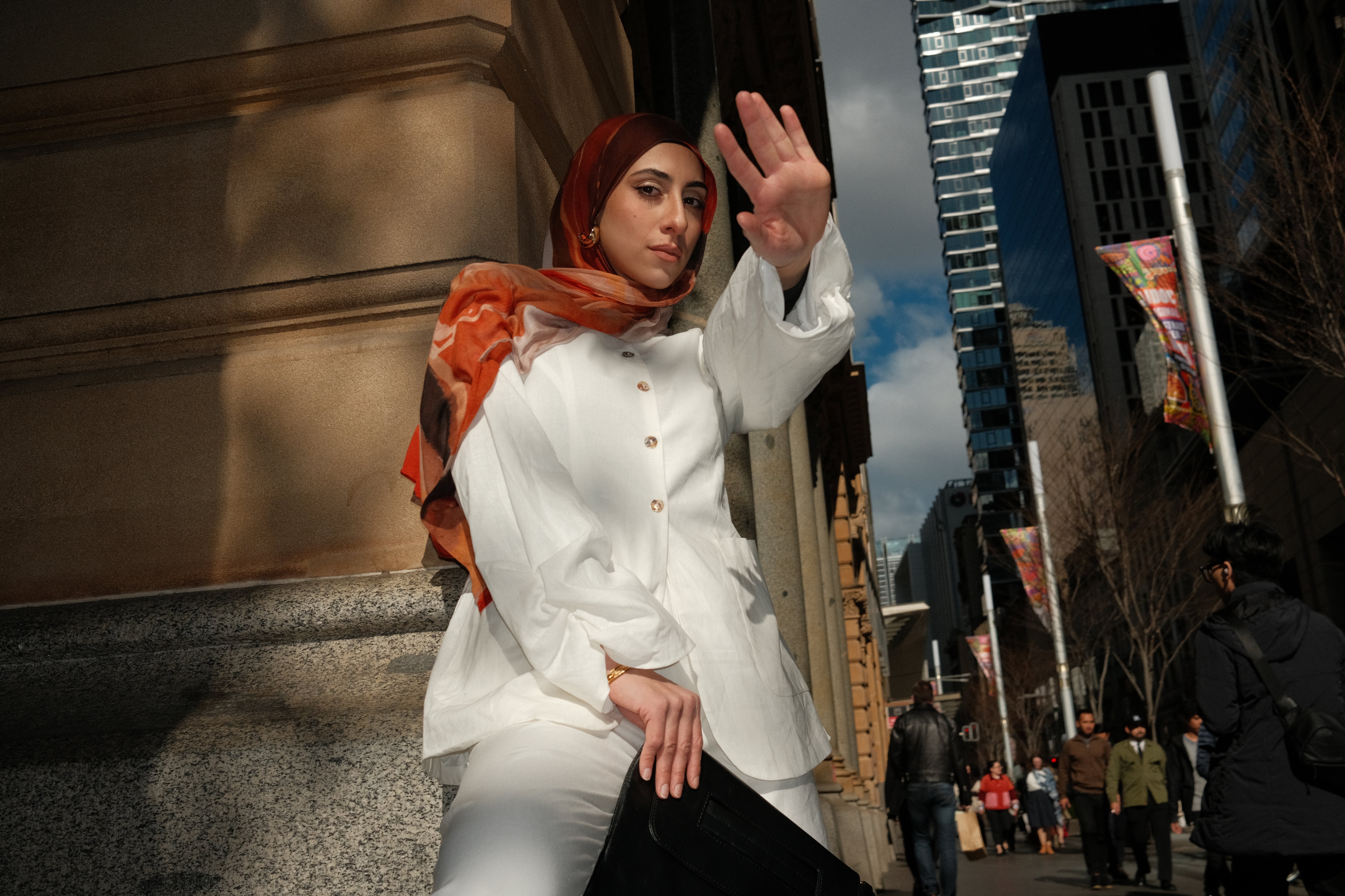 Woman wearing a rust-toned hijab styled with a white modest top, photographed in a city street setting