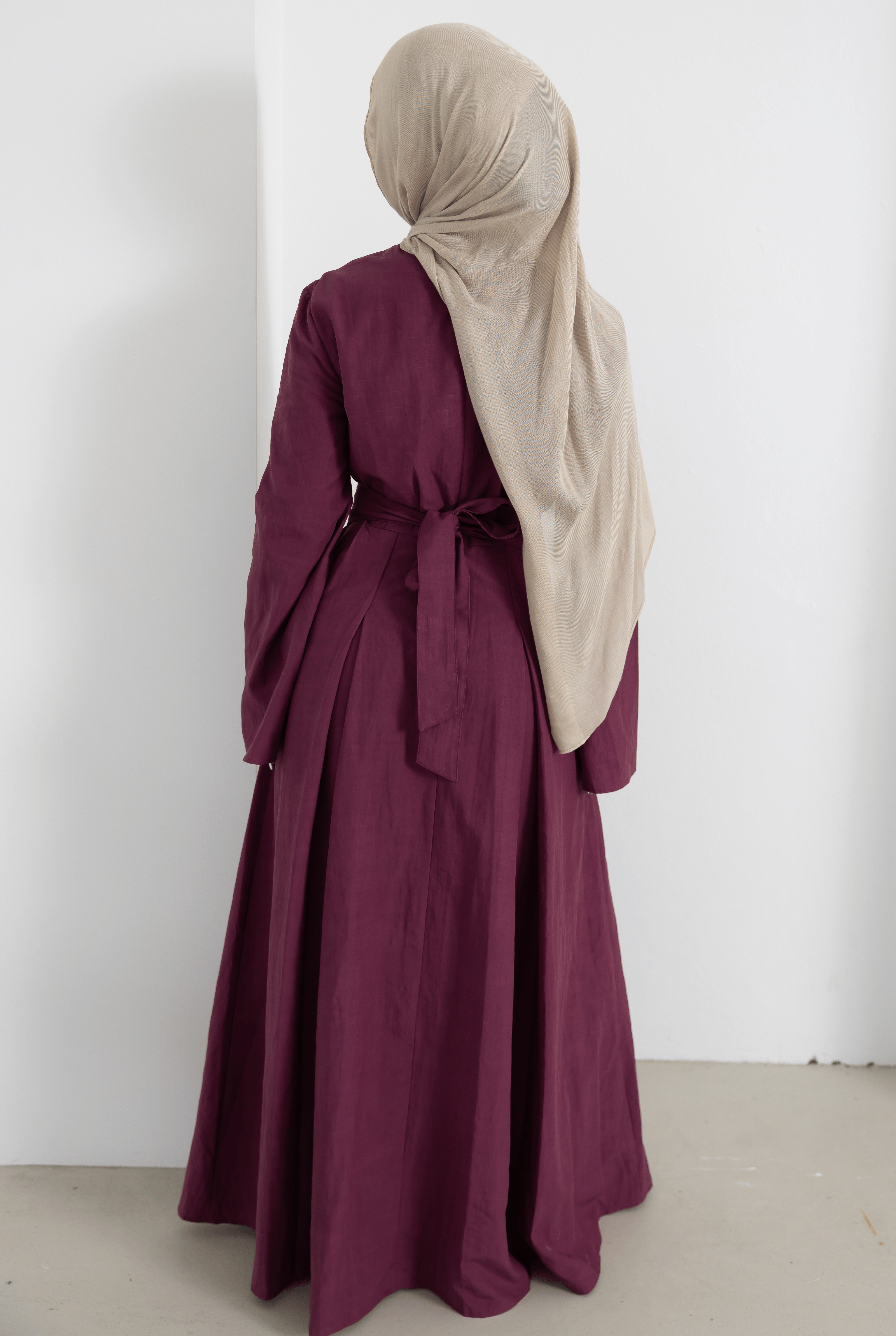 Back view of the Sorelle Belted Dress in plum, featuring a matching waist tie belt, full-length modest silhouette, and flowing lyocell-linen blend fabric. Designed with soft movement, elegant drape, and timeless modest styling for everyday wear and special occasions.