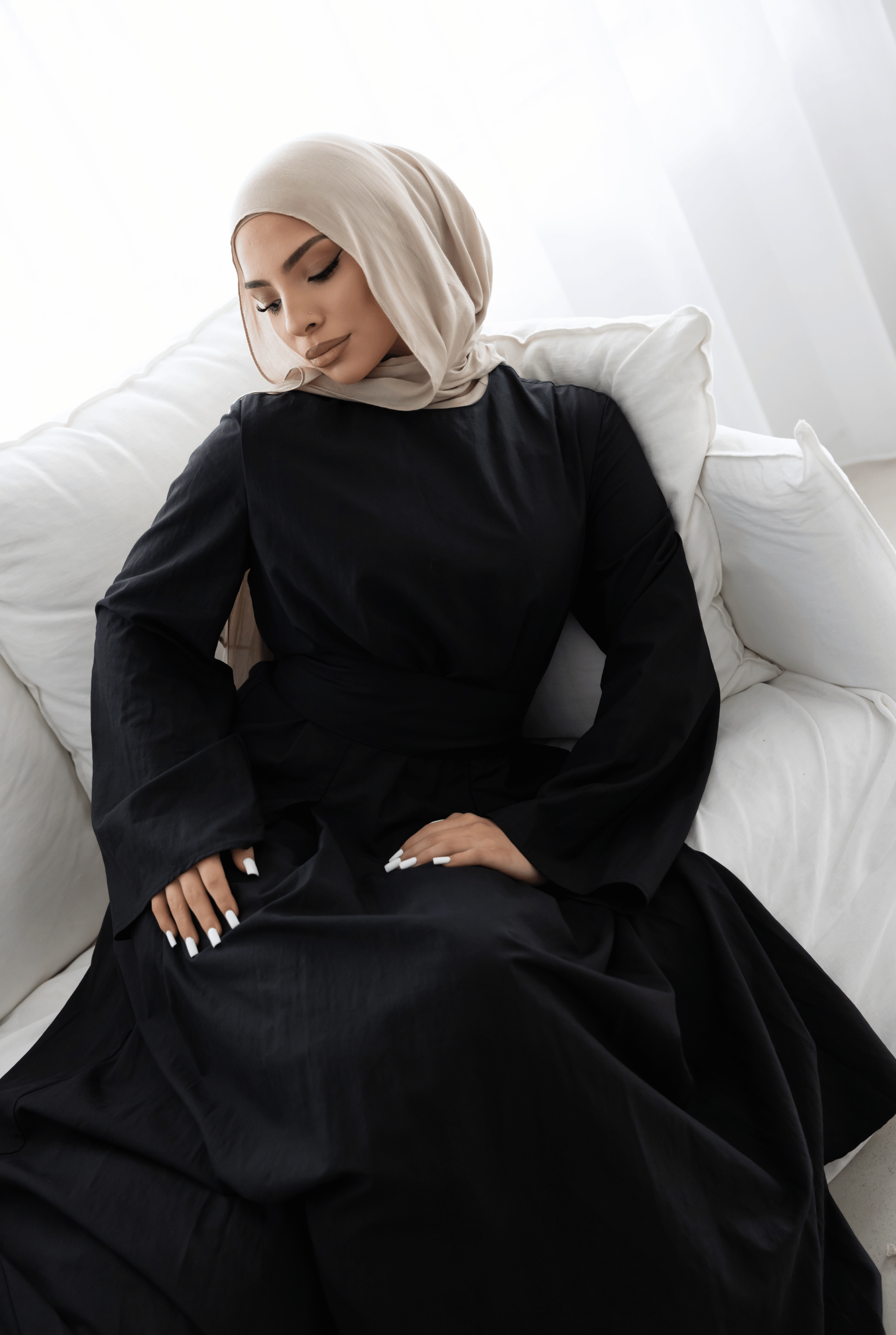 Seated editorial portrait of the Sorelle Belted Dress in black, featuring a flowing full-length silhouette, elegant long sleeves, and a flattering wide waist belt. Crafted from a breathable lyocell-linen blend, this modest maxi dress offers timeless sophistication, comfort, and graceful movement.