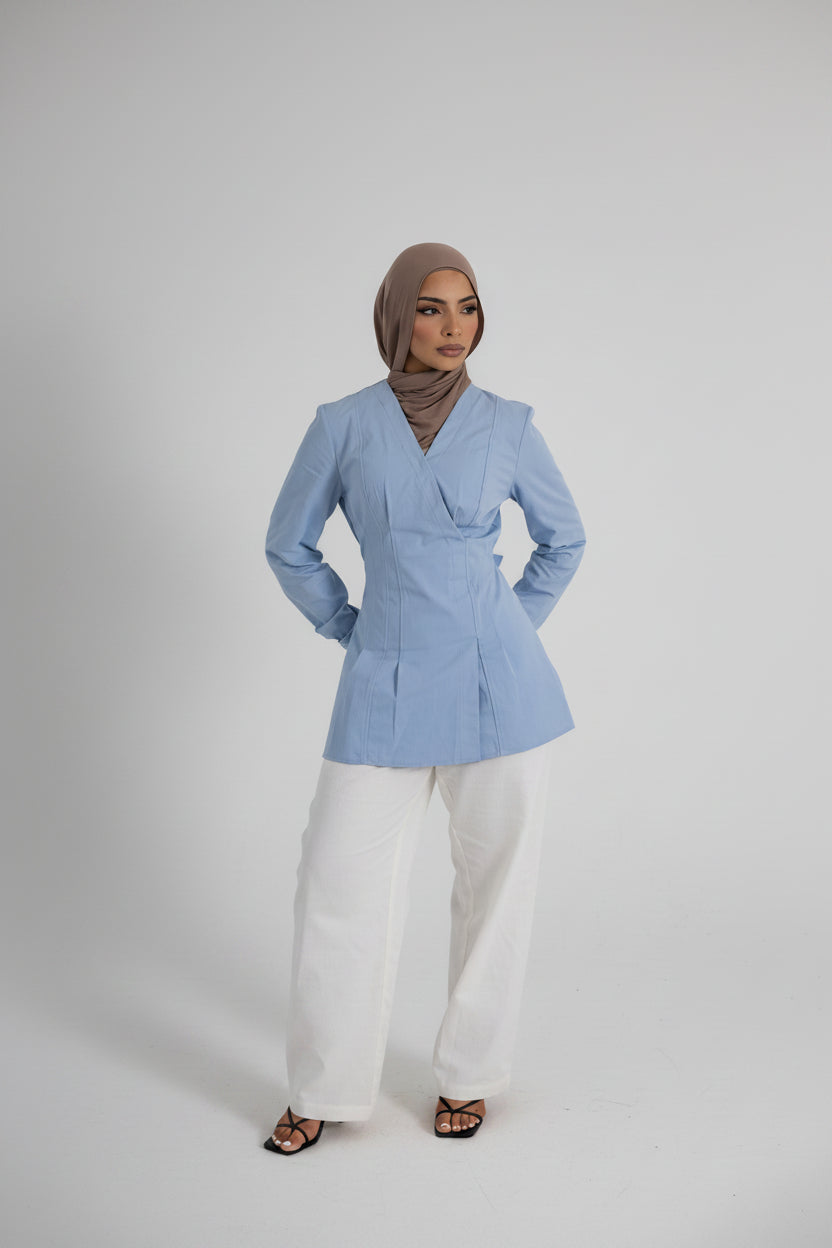 Vellisse Top in blue crafted from 100% cotton, featuring a wrap-style front, adjustable back belt, long sleeves, and a structured tailored fit. Styled with white wide-leg pants and black strappy heels, creating an elegant modest fashion look. Comfortable and versatile women's cotton top designed for everyday wear, workwear, and elevated casual styling.