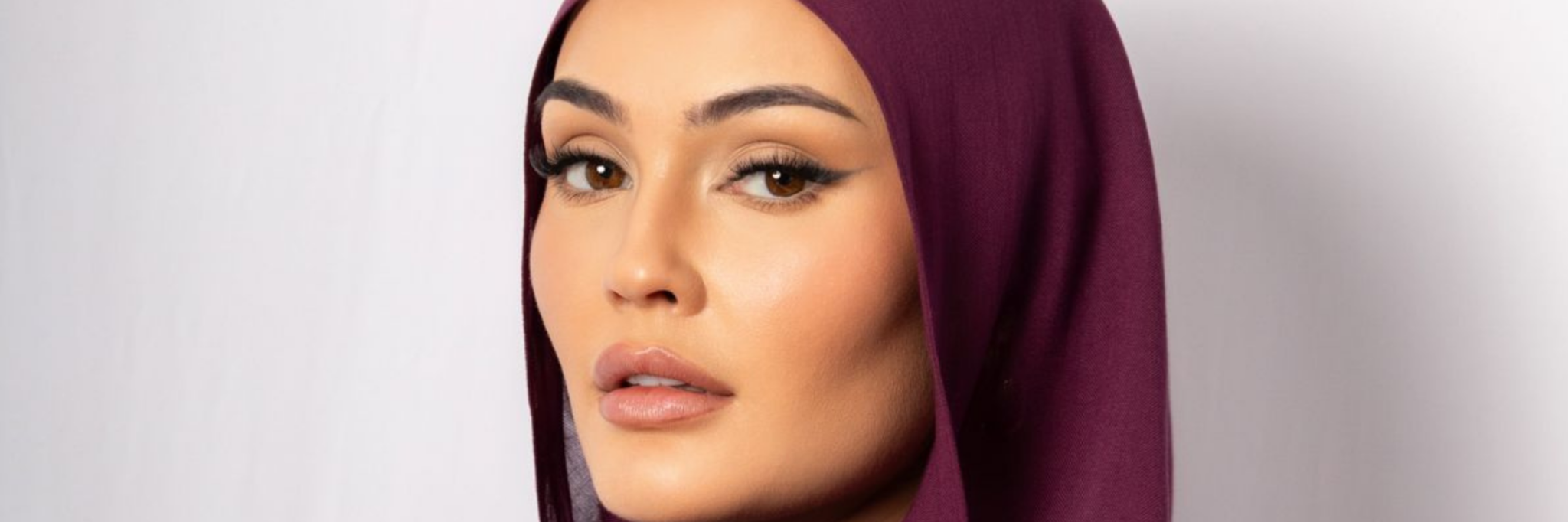 Woman wearing a deep plum hijab posing gracefully with flowing fabric, showcasing elegant modest fashion on a clean studio background