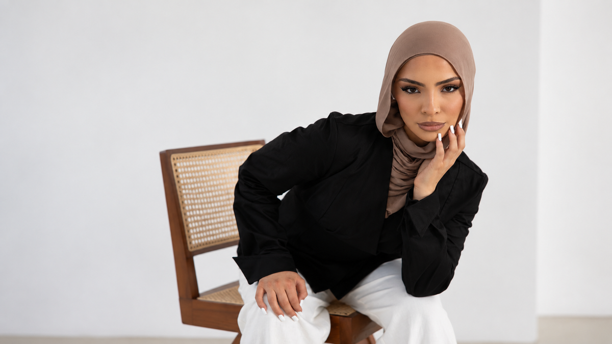 Woman wearing the Vellisse Top in black with a taupe hijab and white trousers