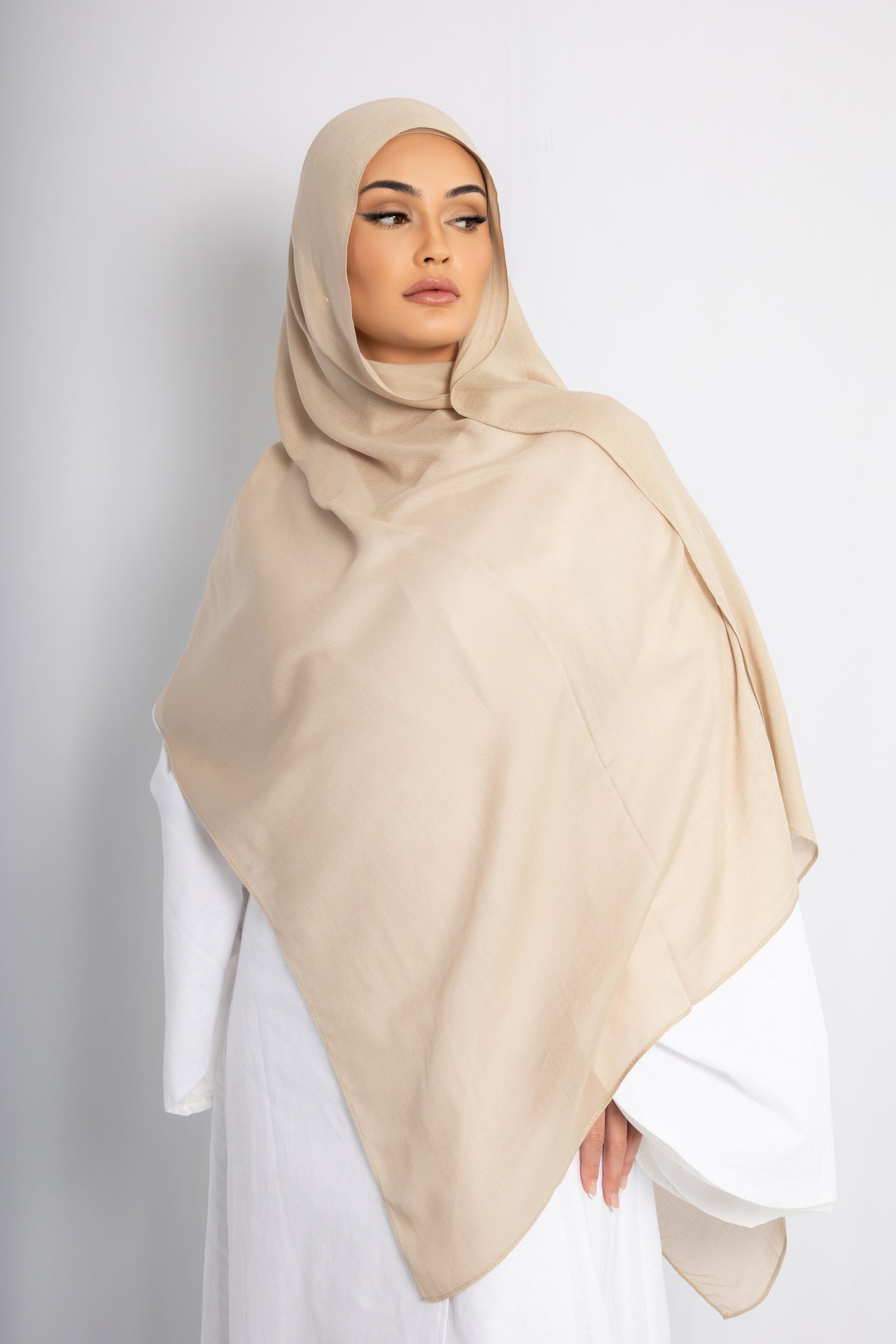Woman wearing a beige hijab styled in a soft, elegant modest fashion look against a clean studio background