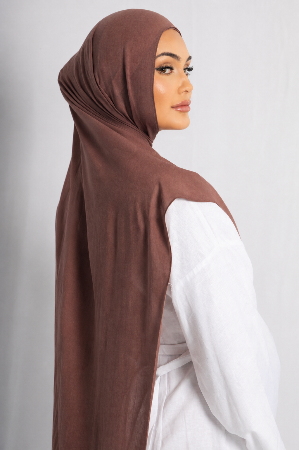 Back view of a model wearing the Cinnamon modal hijab, highlighting its warm cinnamon brown shade, lightweight breathable fabric, long elegant drape, and graceful modest styling