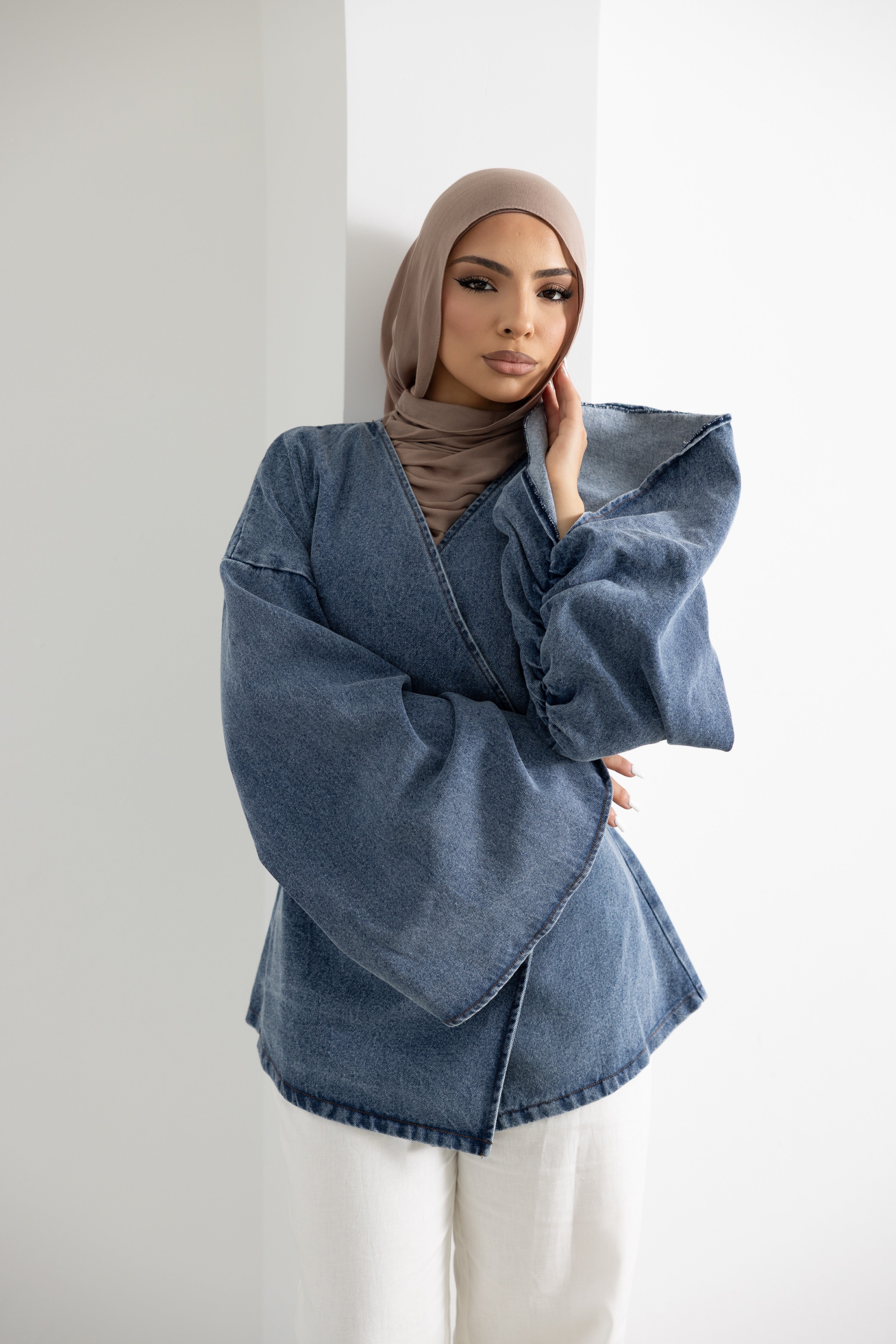 Model wearing the Orlena Signature Denim Mini wrap jacket in blue denim-look cotton fabric. Features a wrap-style front, wide sleeves, back tie waist detail, mini-length silhouette, and modest layering design. Stylish and versatile women's denim jacket for pairing with wide-leg pants, skirts, and everyday modest fashion outfits.