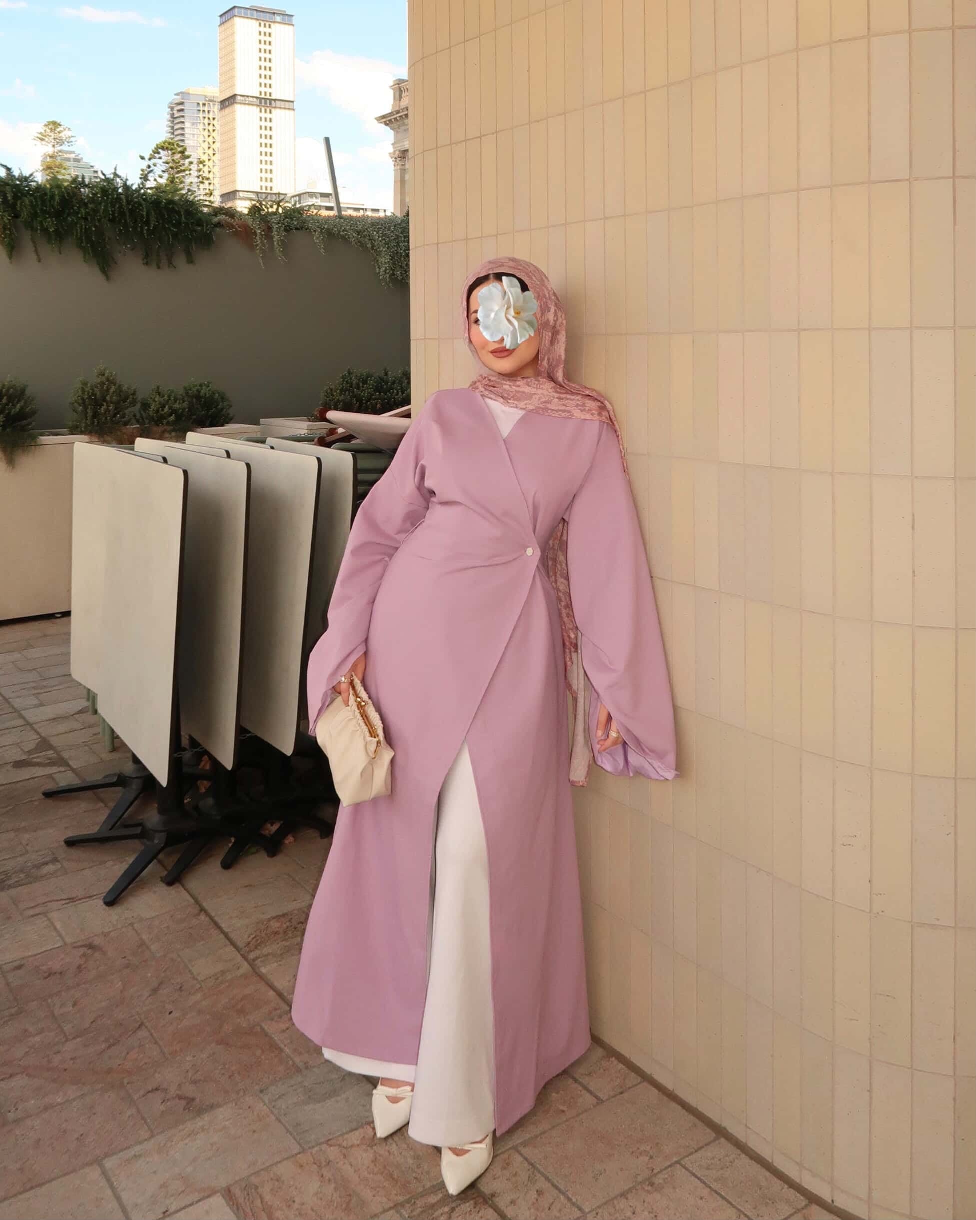 Woman wearing a pink modest wrap dress with patterned hijab and white pants styled as an elegant outdoor city fashion outfit