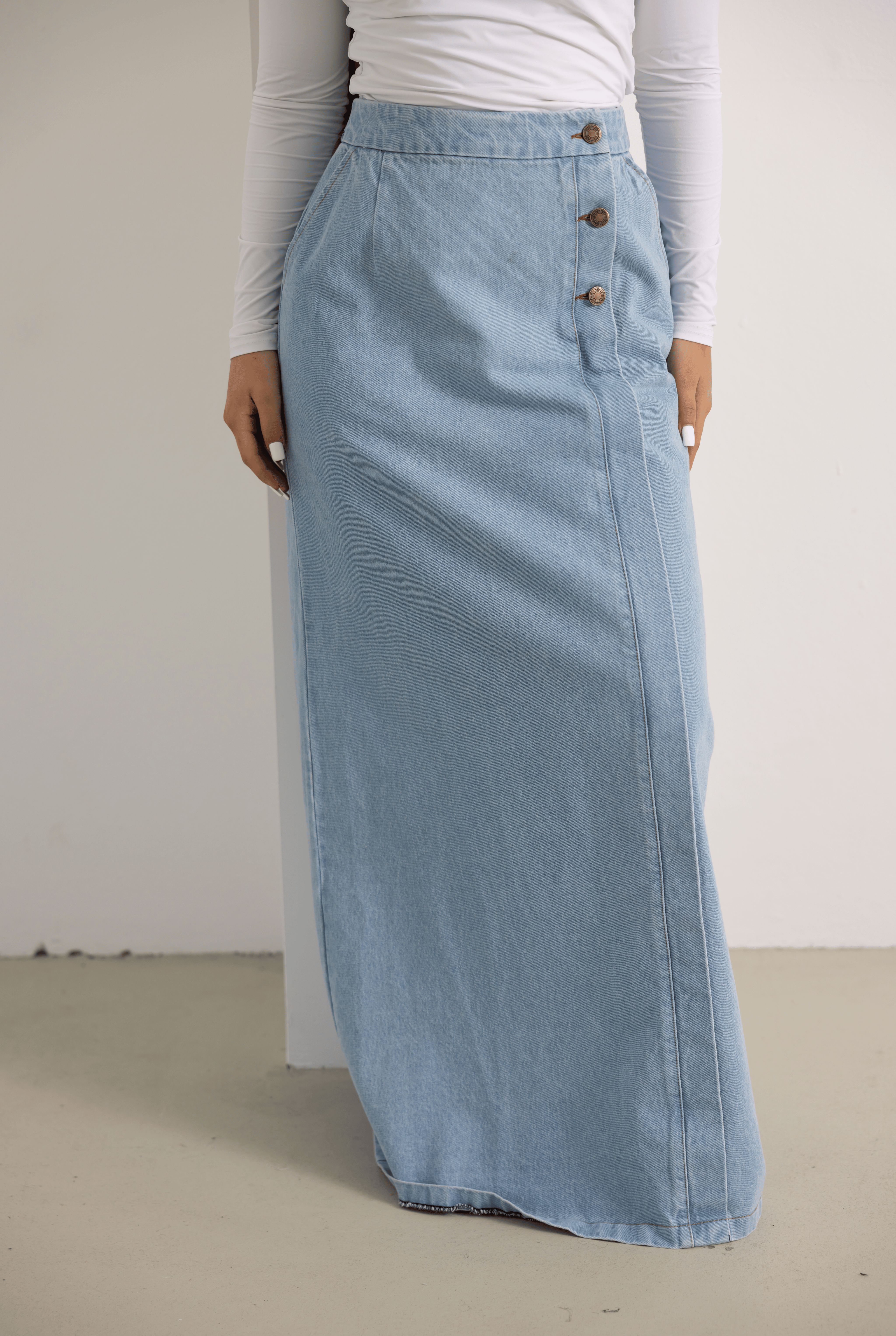 Close-up view of the Side Button Denim Skirt in light denim blue, featuring decorative side button detailing, a modest full-length silhouette, and a soft A-line shape. Crafted from 100% cotton denim for a structured yet comfortable fit, perfect for everyday modest styling.