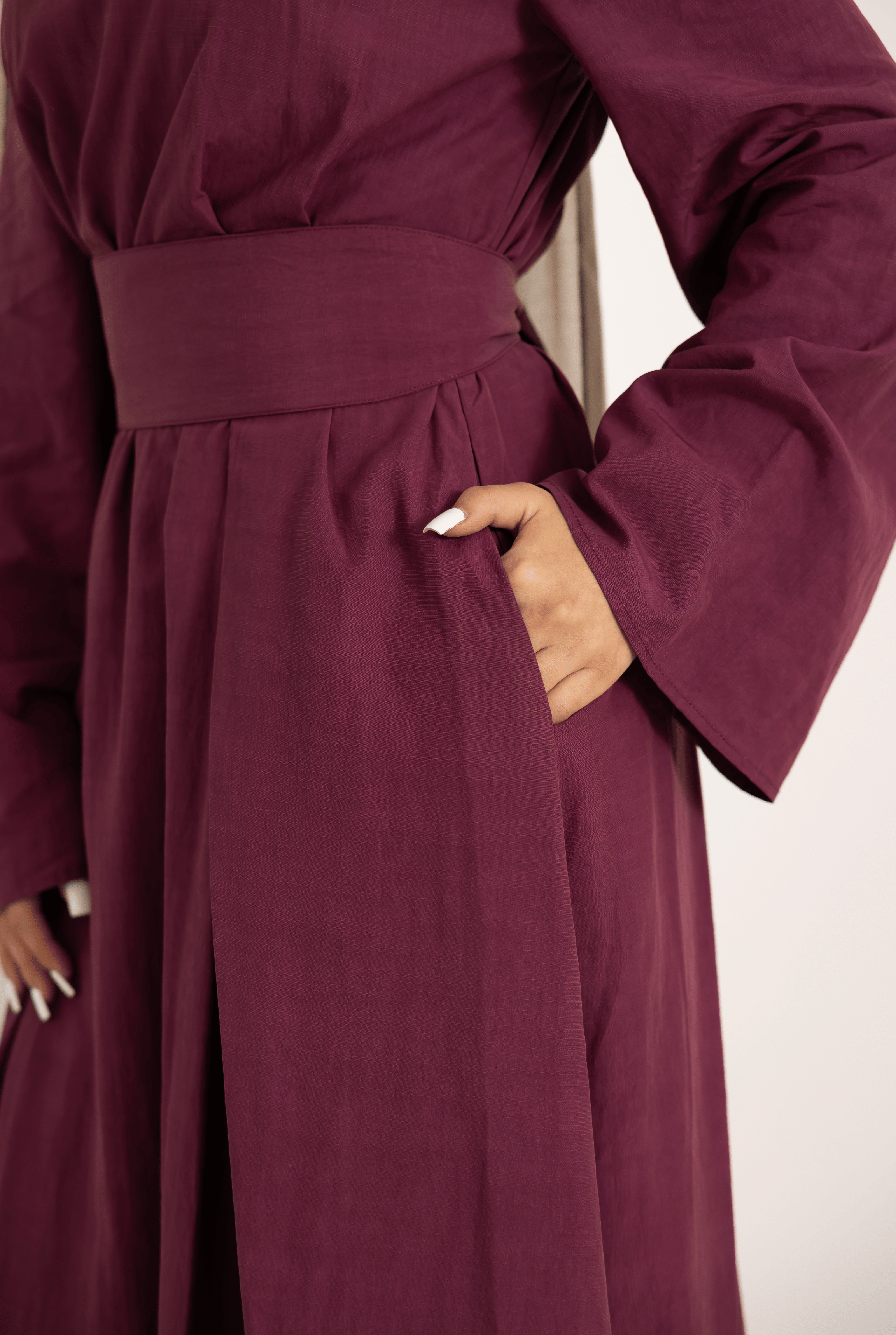 Close-up of the Sorelle Belted Dress in plum, showcasing the matching wide waist belt, flowing full-length silhouette, and soft lyocell-linen blend fabric. Elegant modest dress featuring refined tailoring, wide sleeves, and a flattering feminine shape for everyday sophistication.