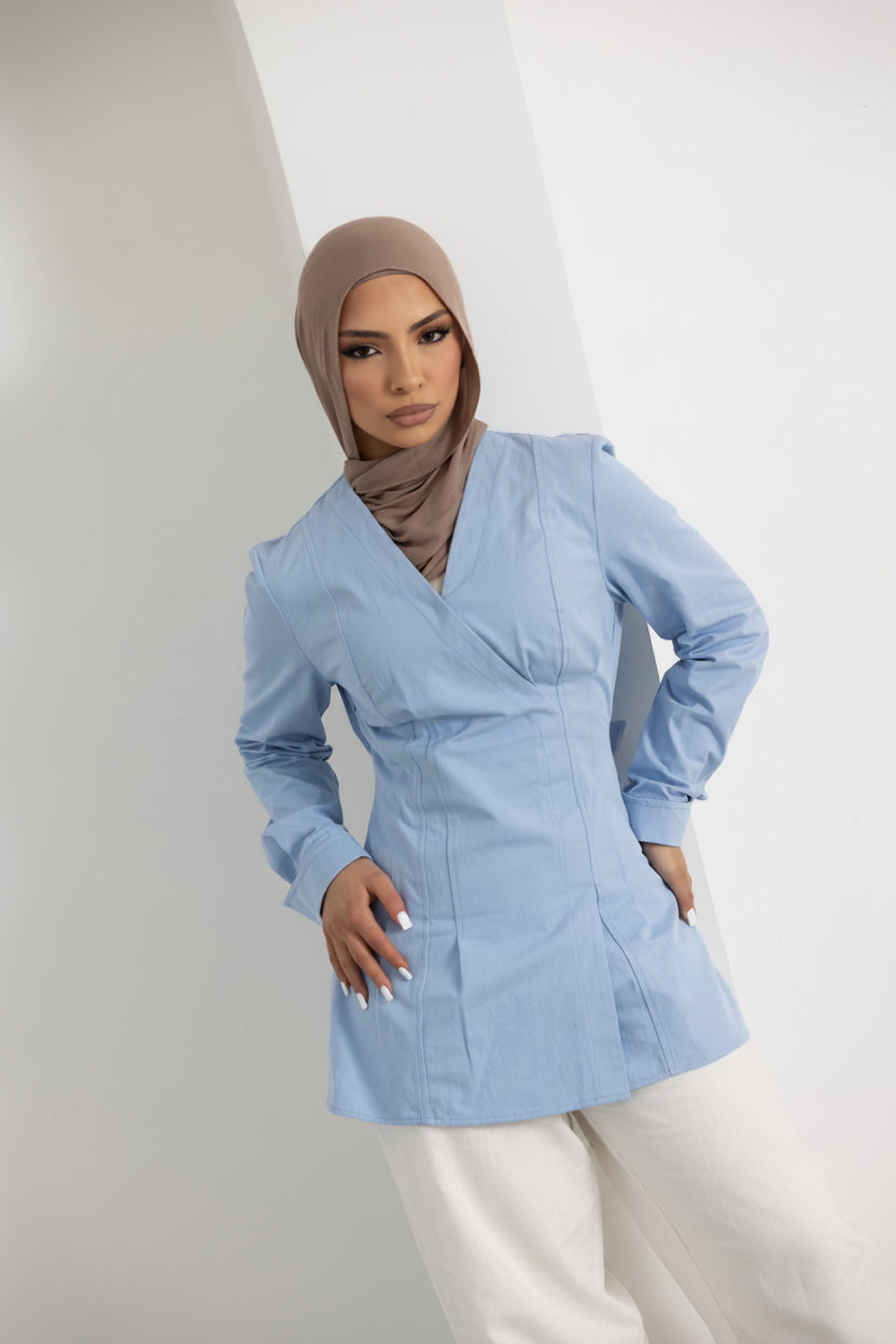 Vellisse Top in blue, crafted from 100% cotton with a structured yet comfortable fit. Features a flattering wrap-style front, long sleeves, and an adjustable back belt to gently cinch the waist. Styled with white wide-leg pants for a polished modest fashion look. Versatile women's cotton top ideal for workwear, casual outings, and elevated everyday styling.
