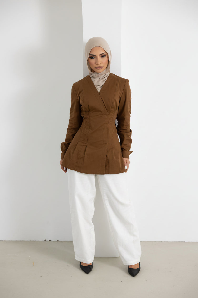 Model wearing the Vellisse Top in brown, crafted from 100% cotton with a structured yet comfortable fit. Features a flattering wrap-style front, long sleeves, and an adjustable back belt to gently define the waist. Styled with white wide-leg pants for a sophisticated modest fashion look, ideal for both casual and elevated everyday wear.